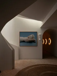 A modern residential hallway with a curved staircase and a framed photograph of a reclining statue on the wall.