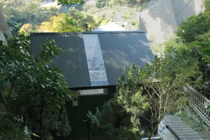 A minimalist house exterior featuring a corrugated metal roof and a long, transparent skylight.