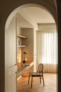 A minimalist home office with a desk, chair, bookshelf, and curtain.