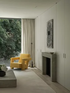 A minimalist living room with a yellow armchair, concrete fireplace, and terrazzo flooring.