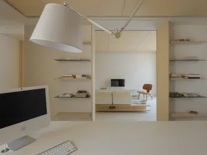 A minimalist living room with wooden shelves containing books, a white sofa, and a television.