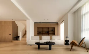 A minimalist living room with wooden elements, including a white sofa, black coffee table, and wooden shelving unit.