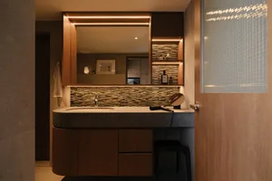 Modern bathroom featuring dark wooden cabinets, a granite countertop, and a large mirror with integrated lighting above. The