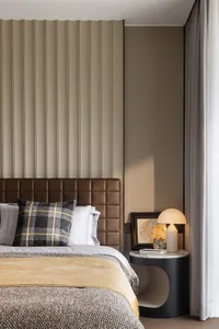 A modern bedroom with a luxurious leather headboard and checkered pillow, featuring a side table with a lamp and framed artwo