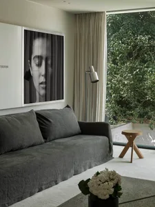 A modern interior design featuring a grey sofa, white curtains, and a minimalist lamp.