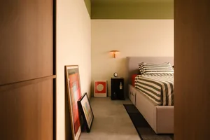 Modern minimalist bedroom with striped bedding and framed abstract art leaning against the wall.