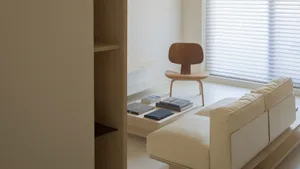 A modern, minimalist living room featuring a simple white sofa, a wooden chair, and a sleek, white console table with several