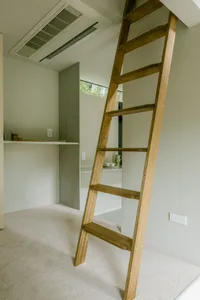 A wooden ladder leaning against a wall, leading up to a higher shelf or storage area.