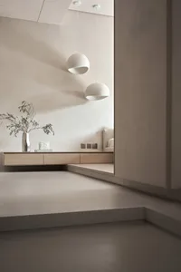A minimalist living room featuring concrete walls and flooring, with two spherical pendant lights hanging above.