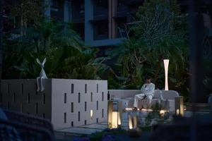 A minimalist living room with a concrete element as the centerpiece, surrounded by lush greenery and modern furniture.
