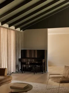Minimalist living room with a wooden piano, brown leather sofa, and metal-framed armchair.