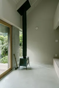 A minimalist residential interior featuring concrete walls, a wooden floor, and a metal structure with a black chimney.