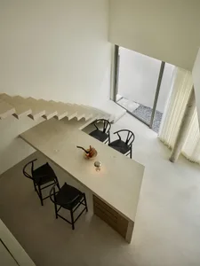 A modern kitchen with a concrete countertop, black chairs, and a bowl of fruit.