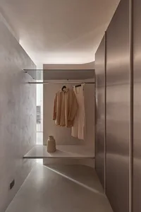A modern minimalist closet featuring a clothing rack and a single vase on a shelf.