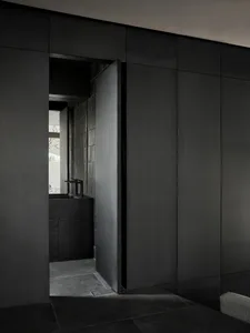 Modern minimalist bathroom with black walls and concrete tiles, featuring a sleek sink and small window.