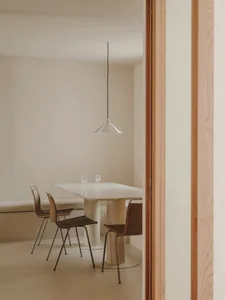 A minimalist dining area with a marble table and wooden chairs against a neutral wall with a wooden beam