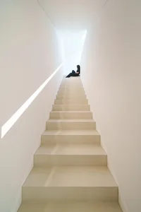 A minimalist staircase with concrete steps, white walls, and natural light