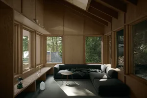 A minimalist living room with wood-paneled walls and large windows showcasing a forested exterior.