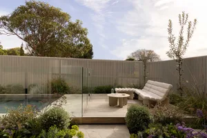 Modern patio featuring wood deck, glass barrier, and greenery.