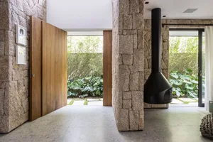 A modern industrial living room with stone walls, a concrete floor, and a black fireplace hanging from the ceiling.