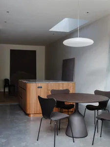 Modern kitchen with wooden dining table, marble countertop, concrete floor, and hanging lamp.