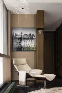 A modern leather armchair on a black marble floor with a painting of running horses above it.