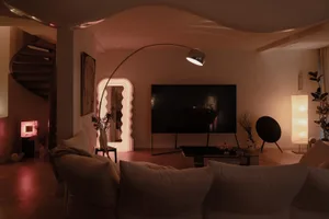 Modern living room with minimalist decor, featuring a curved floor lamp, a television, and comfortable seating.