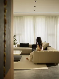 A minimalist living room with a grey fabric sofa, white curtains, and a marble coffee table.