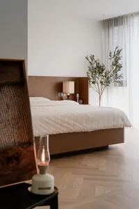A minimalist bedroom featuring a wooden bed and a large window with sheer curtains.