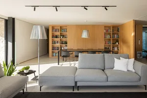 Modern living room featuring a large grey sofa, a bookshelf filled with books, and a dining table.