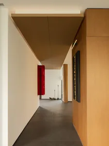 A minimalist hallway with steel and concrete finishes, featuring a wooden cabinet and a red window frame.
