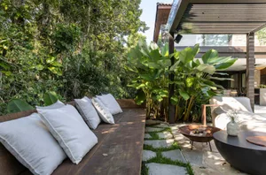 Modern outdoor seating area with tropical plants, wood furniture, and concrete flooring.