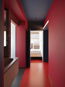 A minimalist bathroom with red tiled floor showing the hallway, doorways, and flooring.