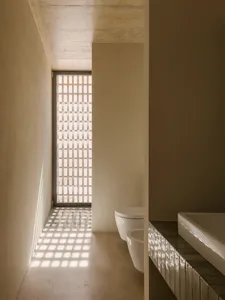 Modern bathroom featuring exposed concrete walls, a sink with a tiled countertop, and a window with a geometric pattern