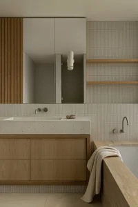 Modern bathroom with concrete countertop and wooden cabinets, featuring a bathtub with a towel.