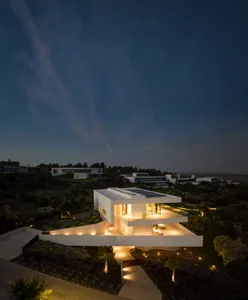 A modern house with concrete and glass exterior illuminated at night.