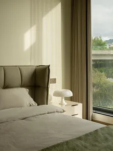 A modern minimalist bedroom featuring beige upholstered headboard, white nightstand, and green throw blanket.