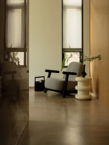 A minimalist monochrome living room with wooden floors and white walls, featuring a checkered armchair, side table, and plant