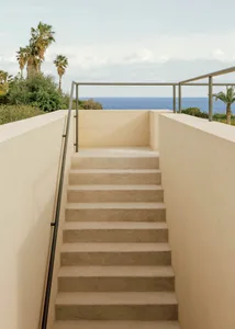 An exterior staircase with concrete steps and railings overlooking the ocean with palm trees in the background.