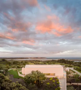 A modern, minimalist house with concrete and glass exterior features a view of the ocean.
