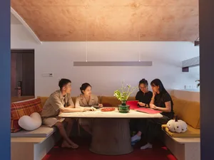 Four people sitting around a round table with a vase of flowers and a red folder in a modern living room with upholstered sea