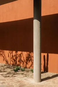 A minimalist exterior design featuring a concrete column casting a shadow on a textured wall.