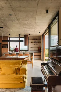 A modern concrete living room with a yellow couch and a piano.
