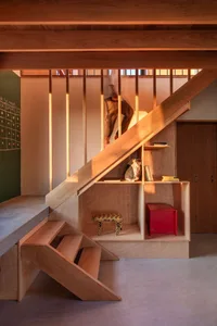 A modern interior featuring a wooden staircase with a built-in shelf containing books and decorative items.