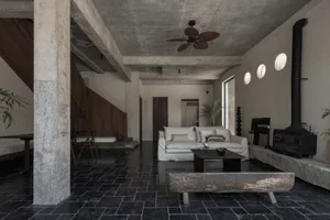 Modern minimalist living room with exposed concrete ceiling and black tiled floor, featuring a white sofa and a wooden coffee