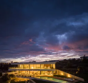 Modern residential exterior with a glass and concrete facade illuminated during the evening with the sky in the background.