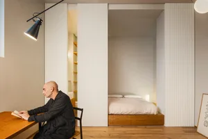 A minimalist bedroom featuring sliding white walls and a wooden platform bed.