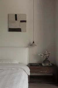 Minimalist bedroom with white bedding and a wooden nightstand.