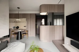 A minimalist living-dining room with wooden panels, featuring a sofa, a small round dining table, and a television.