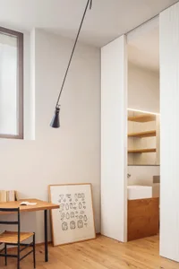 A modern home office with a wooden desk and chair, featuring a hanging lamp and a framed illustration.